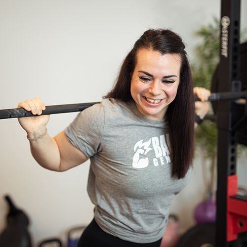 Amela Bajramovic legitimerad naprapat på Smood Malmö står med skivstång på axlarna på gymmet