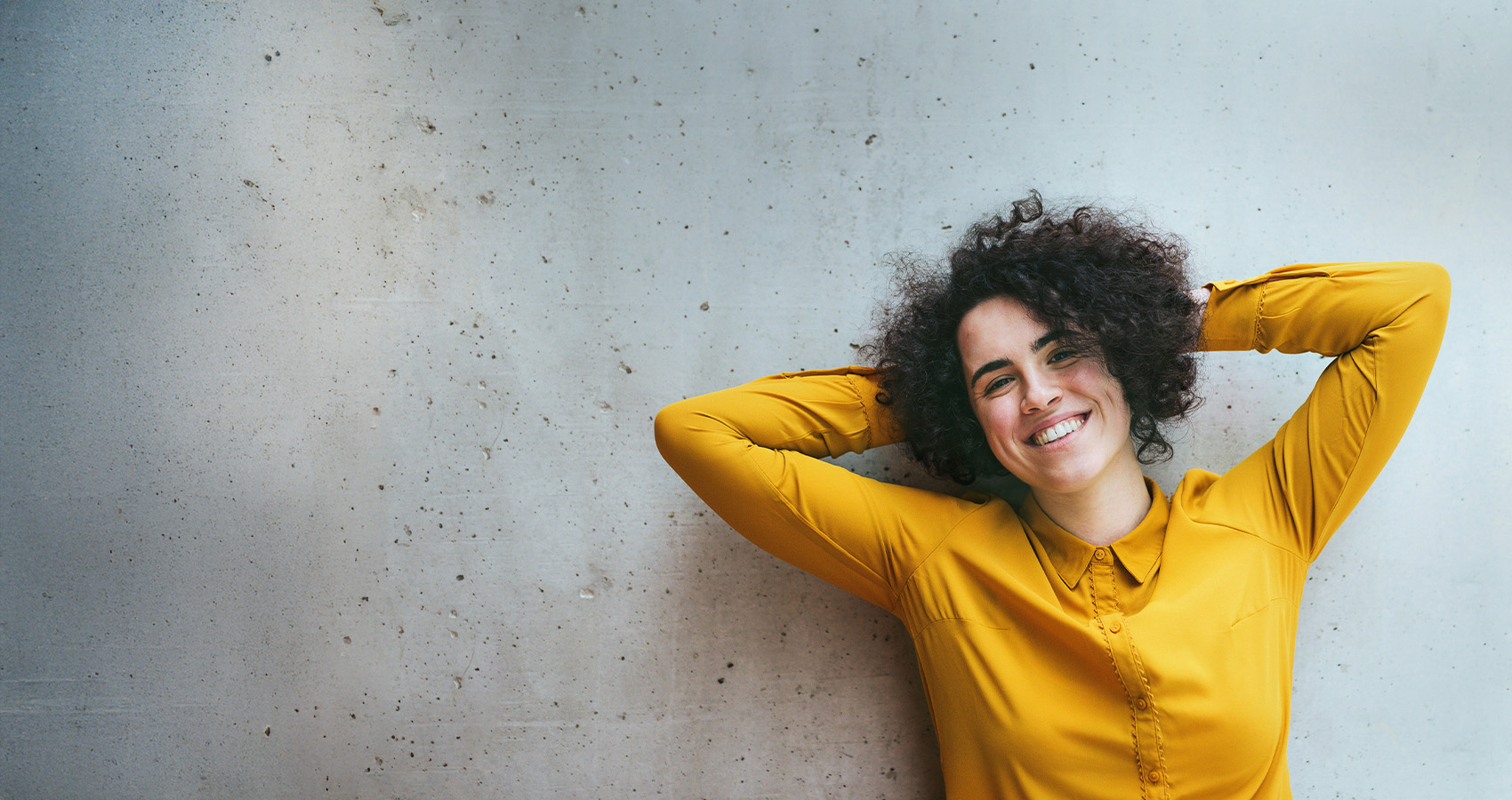 Glad tjej med gul skjorta står framför en grå betongvägg